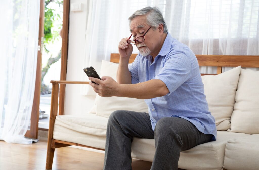 Older person sits on a couch struggles to see the phone in their hand, due to AMD.