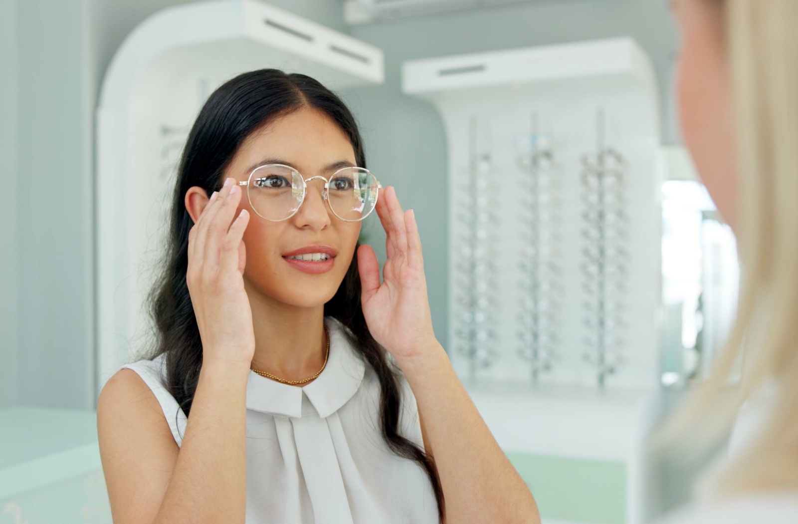 A person trying on a new pair of glasses and looking at an optician who is helping them