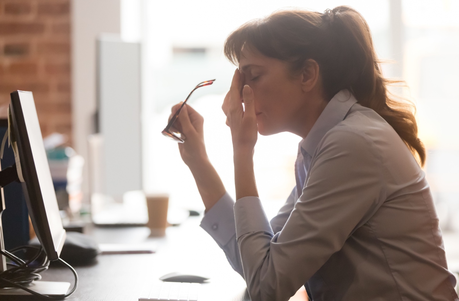 A person with blurry vision removes their glasses and rubs the bridge of their nose.