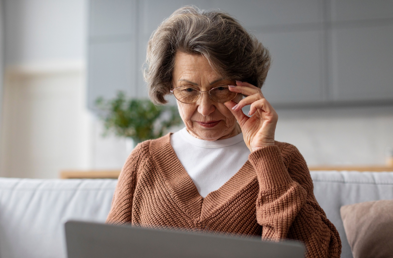 An older adult with AMD adjusts their glasses to try to see their laptop clearly.