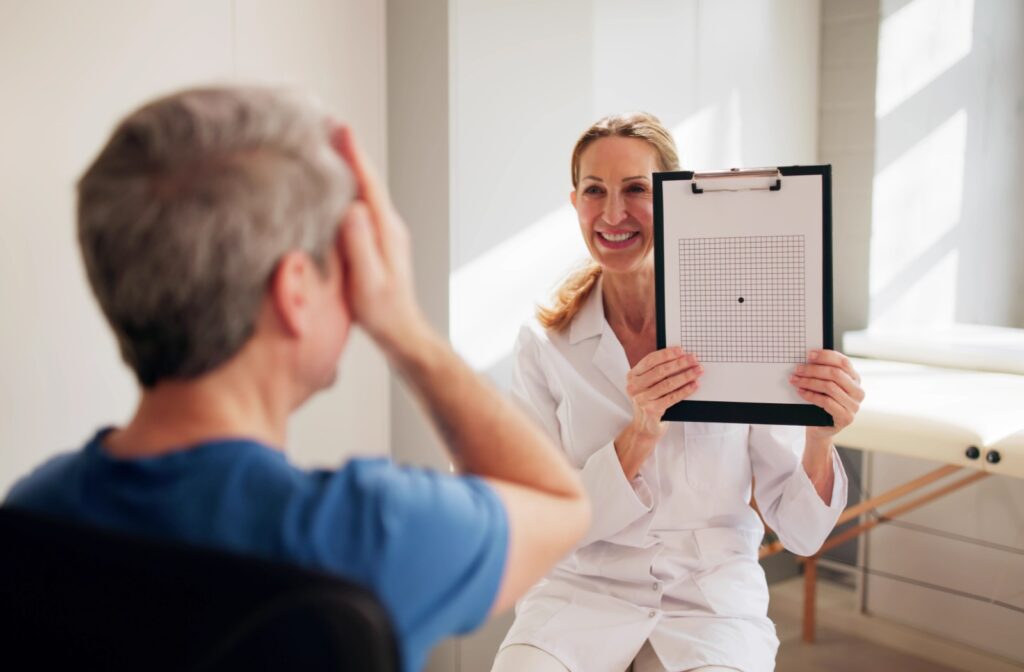 Optometrist holding up an Amsler grid chart while a patient covers one eye during a macular degeneration screening test.