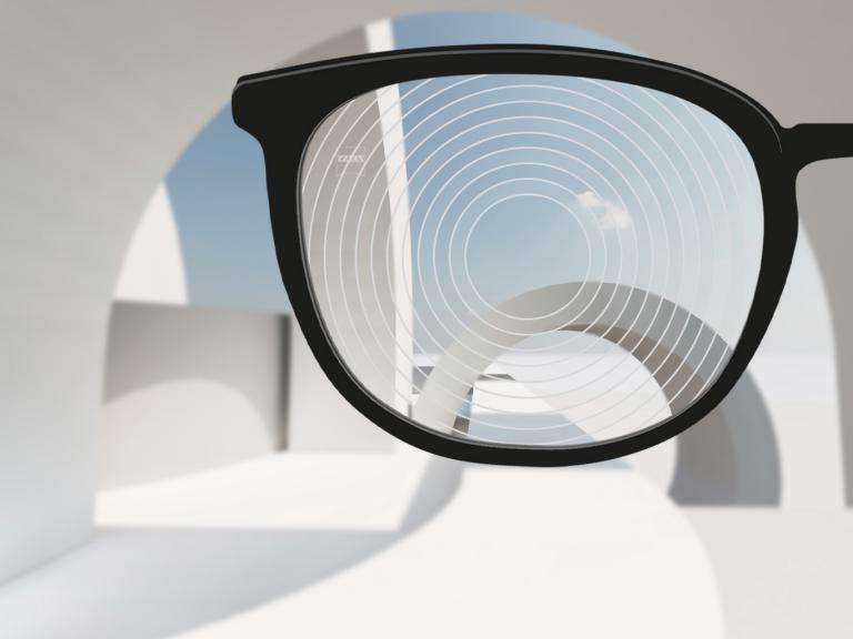 Close-up of black eyeglass frame showing MyoCare lens with visible concentric ring pattern demonstrating defocus zone technology for myopia control on white background.