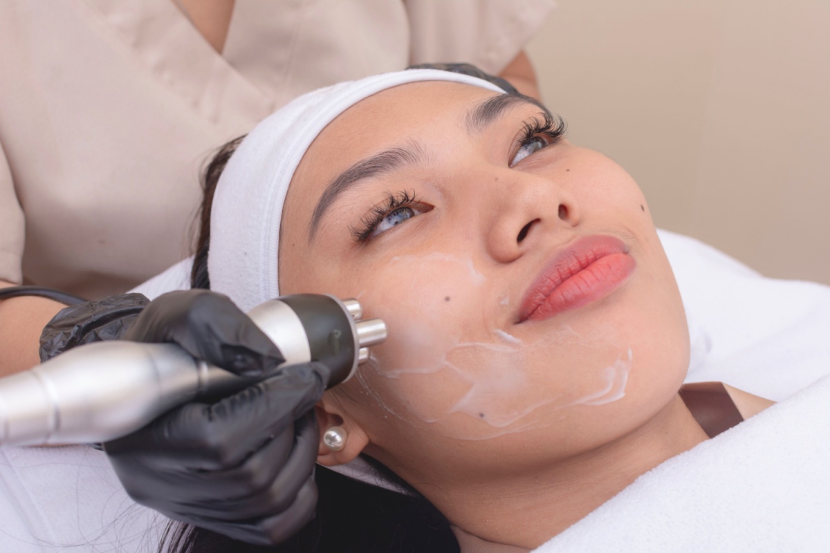 Woman relaxing with while receiving radiofrequency facial treatment with handheld device by aesthetician.