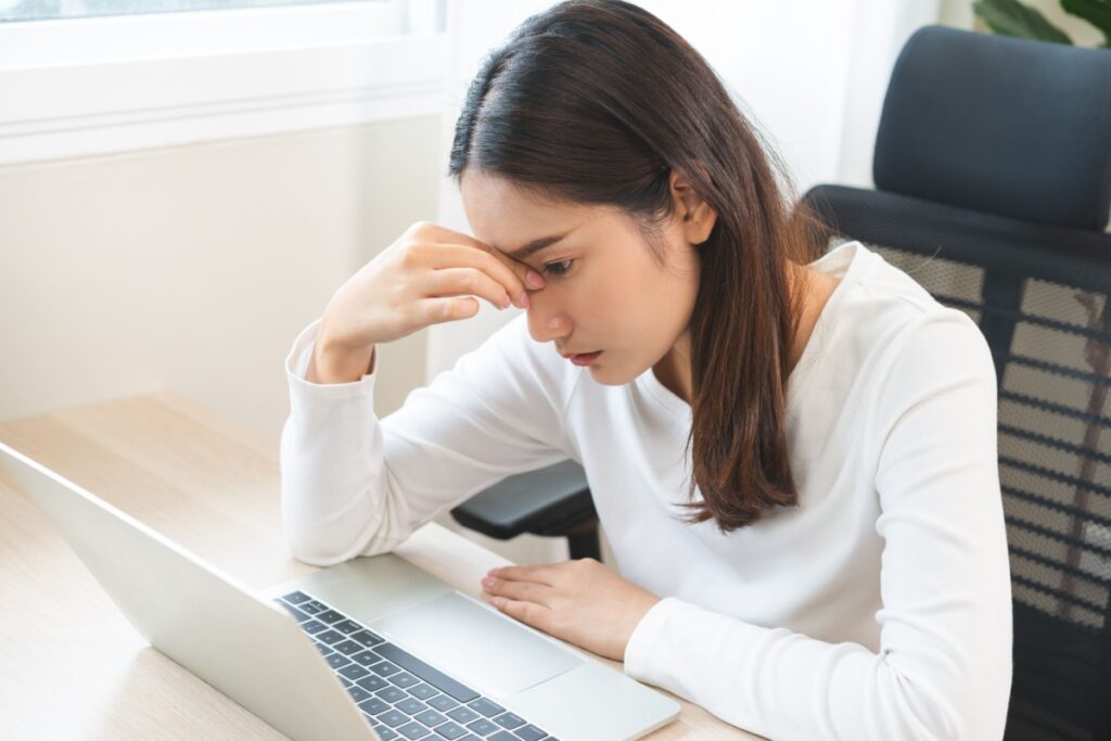 Woman rubbing bridge of her nose from digital eye strain while working on a laptop.